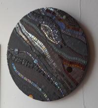 A circular mosaic in shades of black with touches of gold and orange.